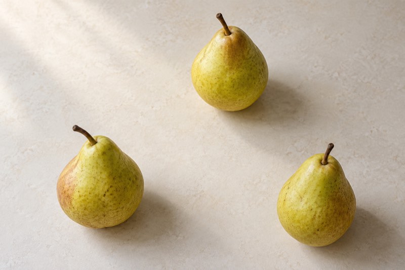 Três peras amarelo-esverdeadas vistas de cima sobre uma mesa creme, formando um triângulo com espaços bem definidos entre elas.